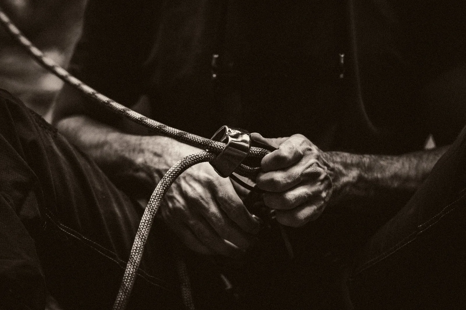 A hand holding a climbing rope threaded through a belay device, in low light.
